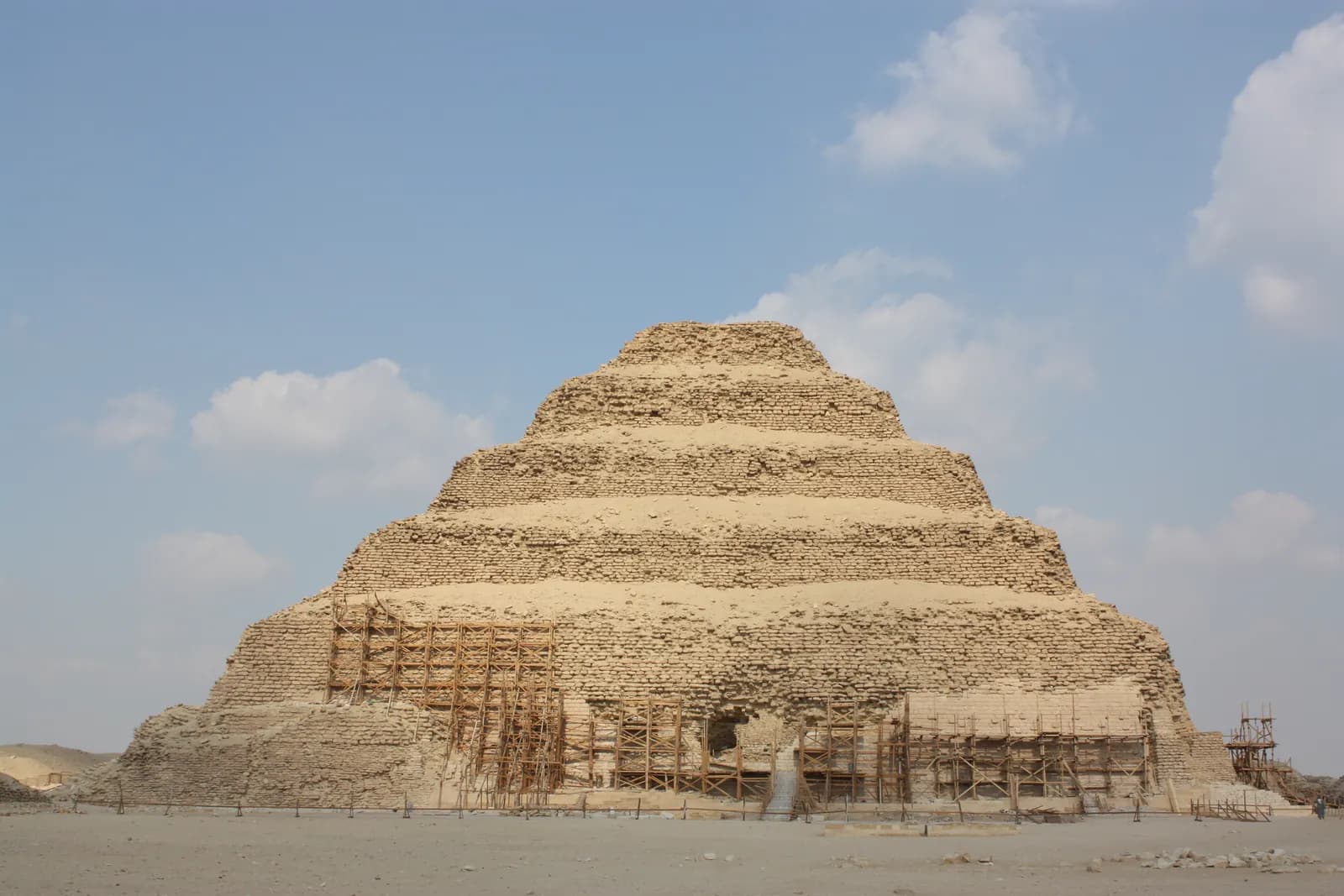 Stepped pyramid of six diminishing stone tiers rising from desert sand.