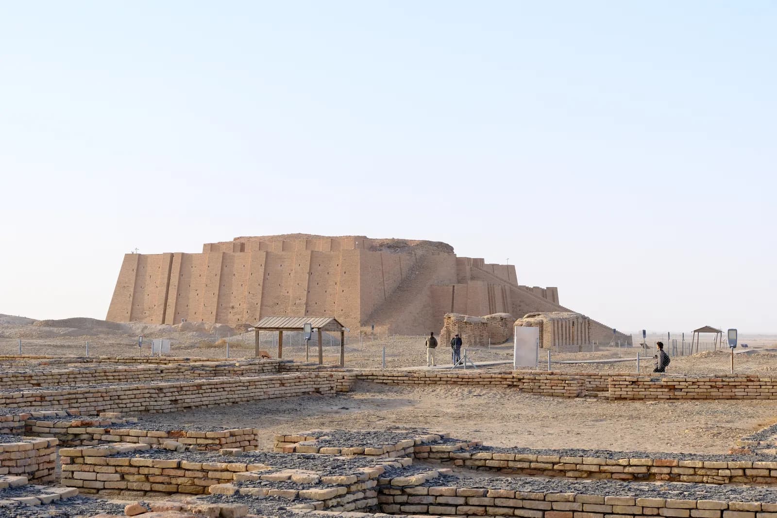 A massive stepped brick platform in flat desert, with three long converging stairways climbing its front to a landing.