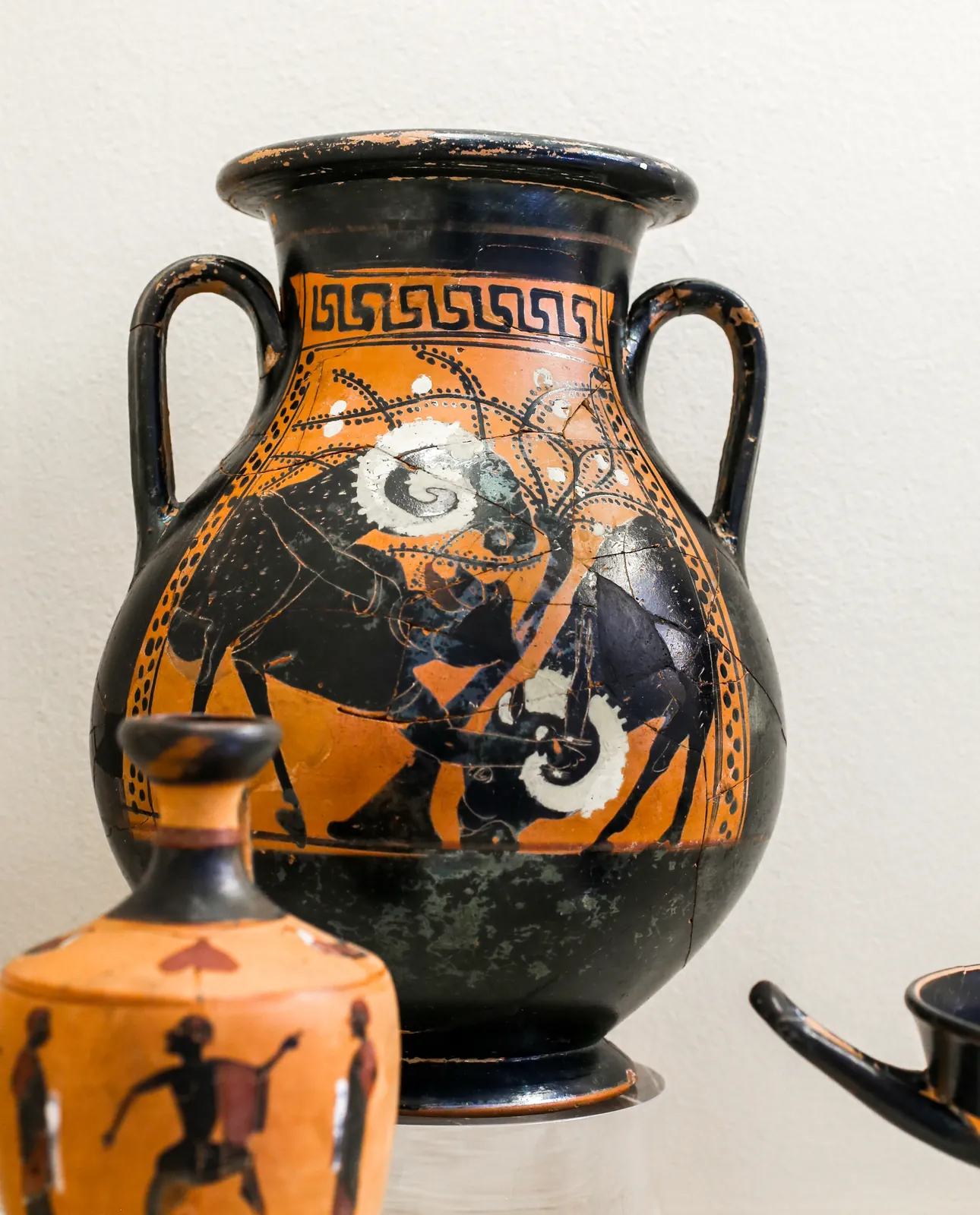 Black-figure vase painting of a bearded man clinging beneath the belly of a large ram as it walks.