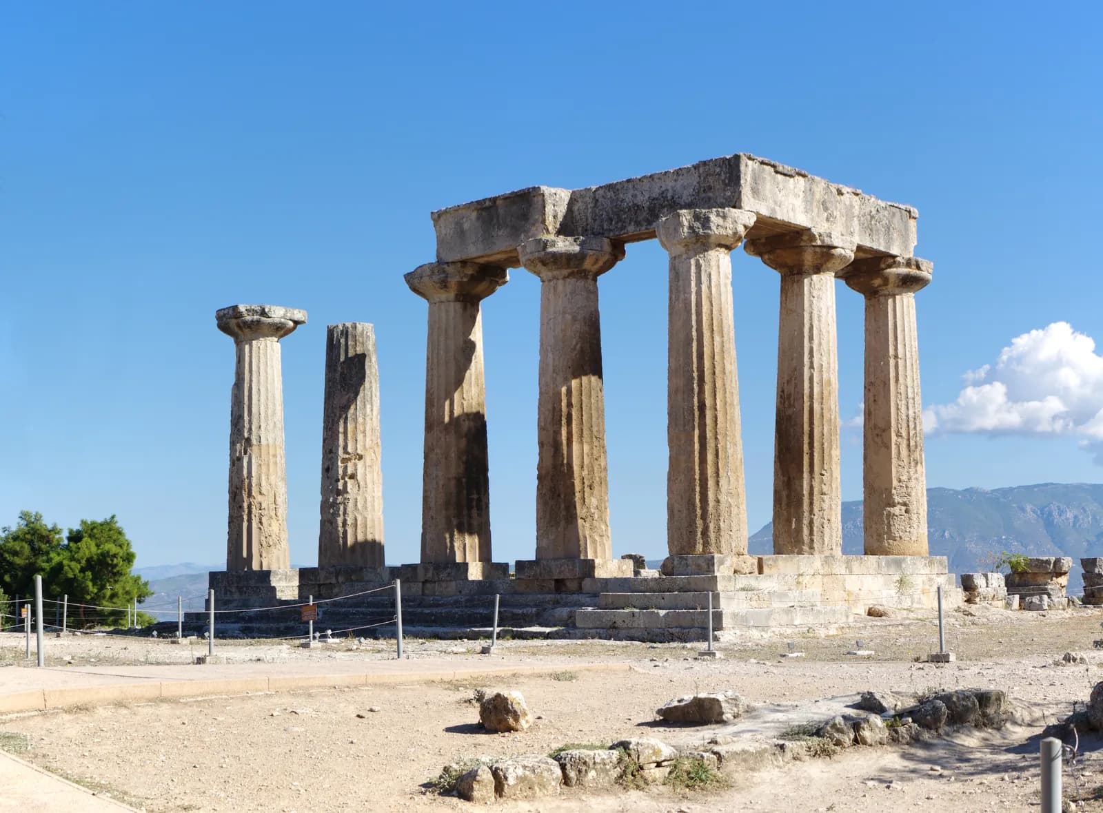 Row of squat monolithic Doric columns standing on a platform, with a steep rock massif rising in the distance.
