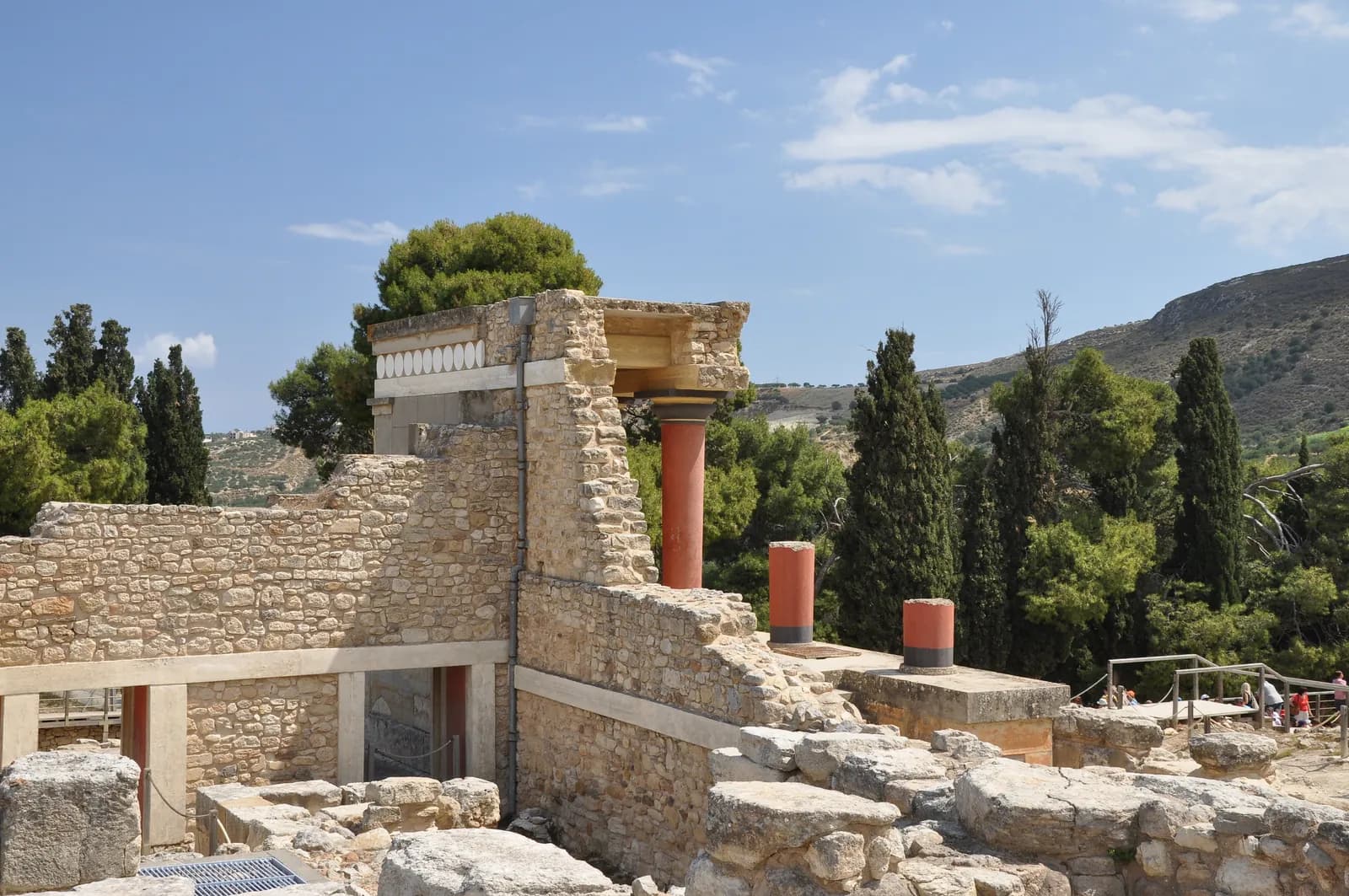 A ramp between walls at Knossos, flanked by red-painted tapering columns supporting a roofed portico, with a large bull fresco panel set into the wall above.