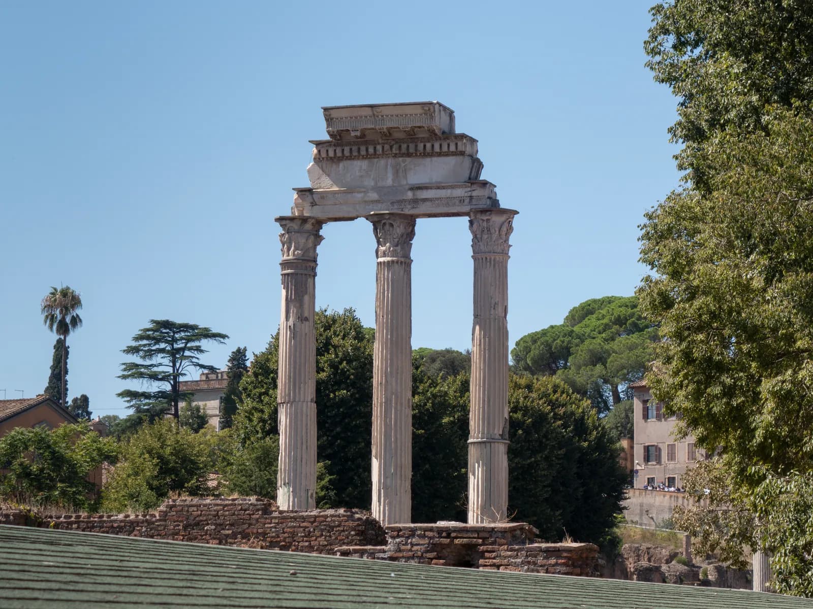 Three tall fluted Corinthian columns standing together and carrying a section of carved entablature, isolated above the Forum.