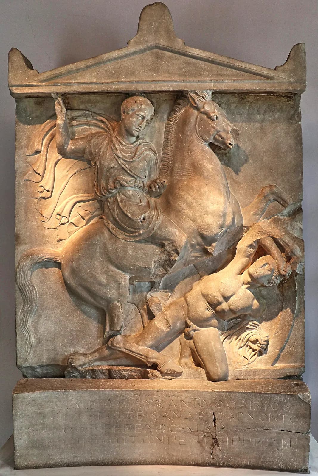 The carved marble grave stele of Dexileos, a young Athenian cavalryman, shown rearing on horseback and spearing a fallen naked enemy beneath him.