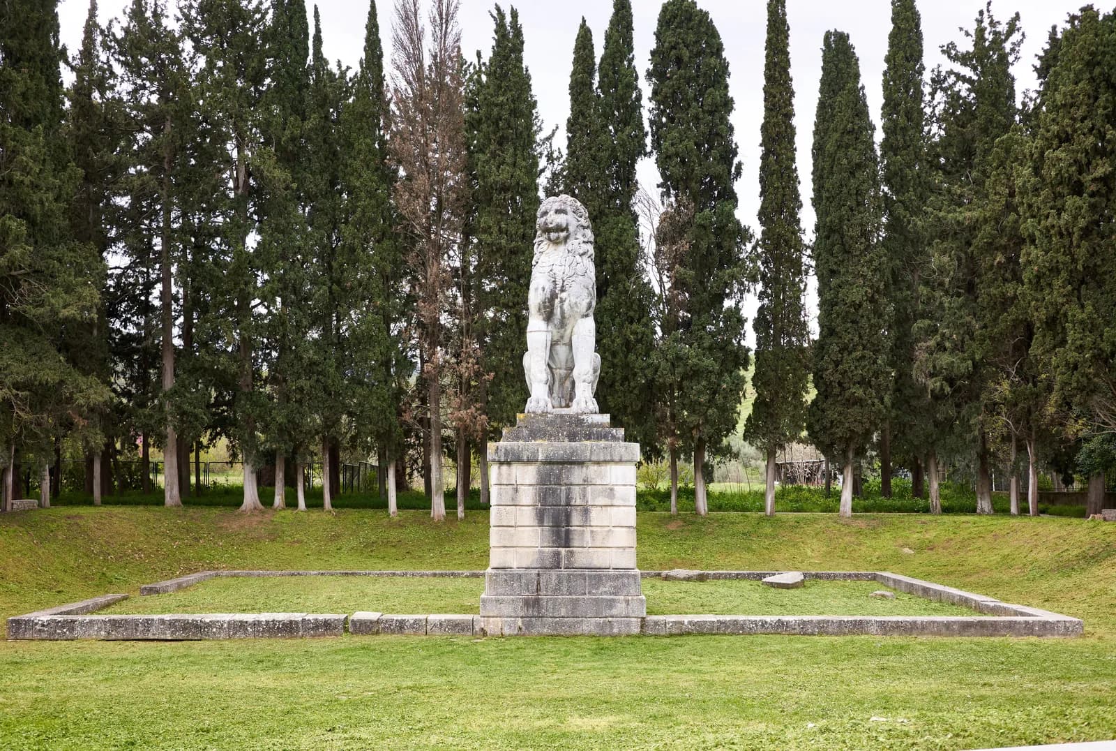 The restored marble Lion of Chaeronea seated on a high plinth in the Boeotian countryside, the funerary monument marking the grave of the Theban Sacred Band who fell at the battle of 338 BCE.