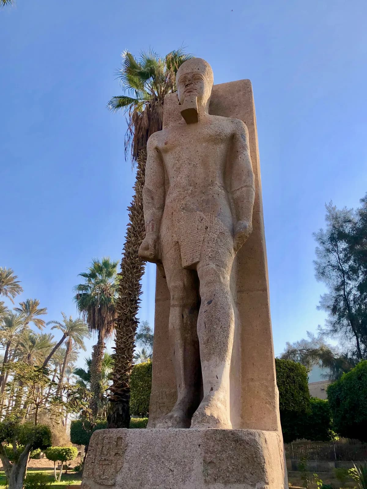 A colossal limestone statue of a pharaoh lying on its back under a shelter, seen from above, with the legs broken away below the knees.