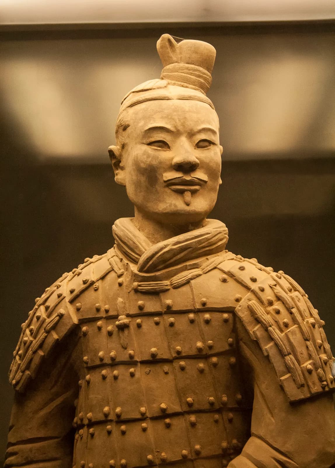 Close view of a single terracotta soldier from the army of the First Emperor — an individually modelled face, topknot and armoured torso, each figure made distinct.