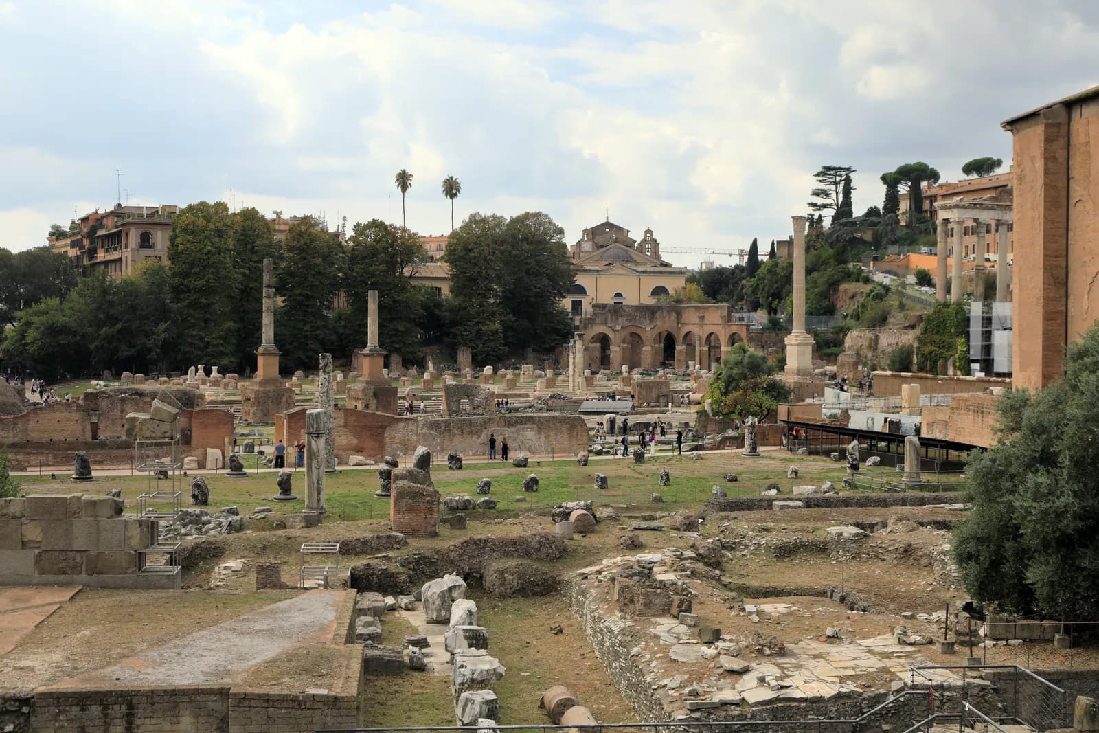 A wide marble pavement bounded by rows of low brick pier stumps, with the standing columns of the Forum behind.