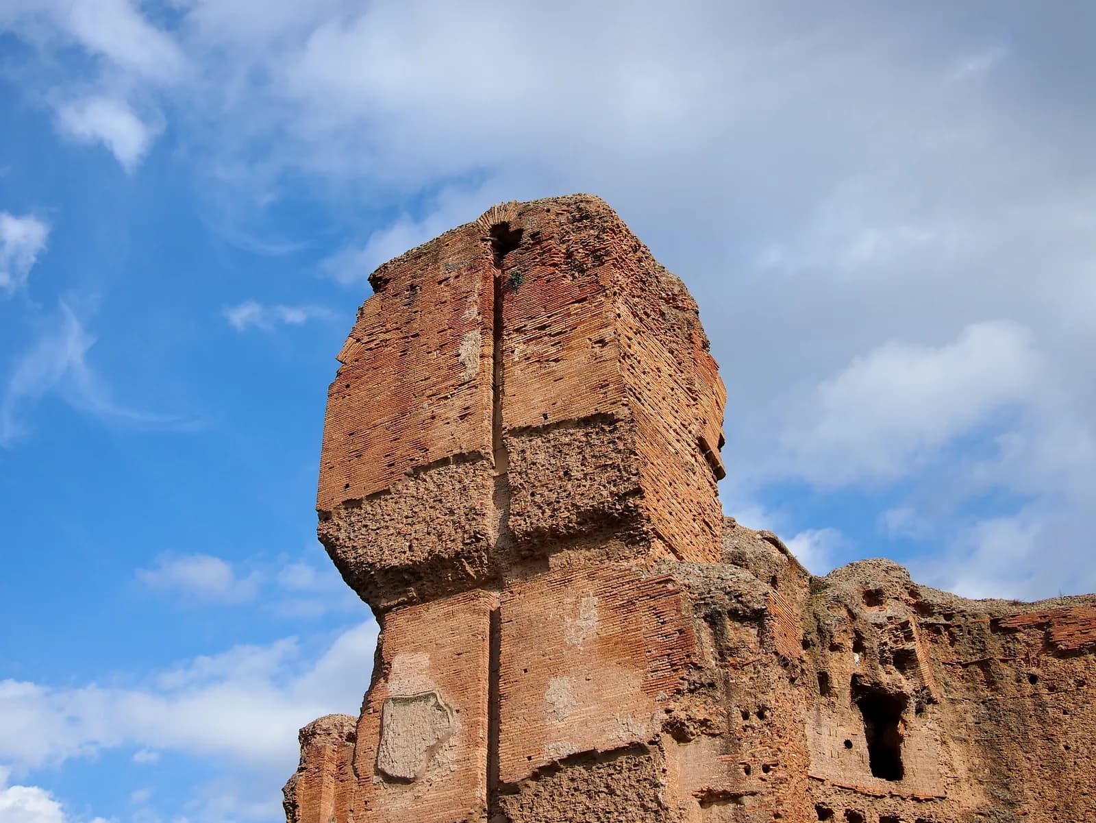 Towering roofless walls of brick-faced concrete pierced by great arched openings, stripped of every surface.