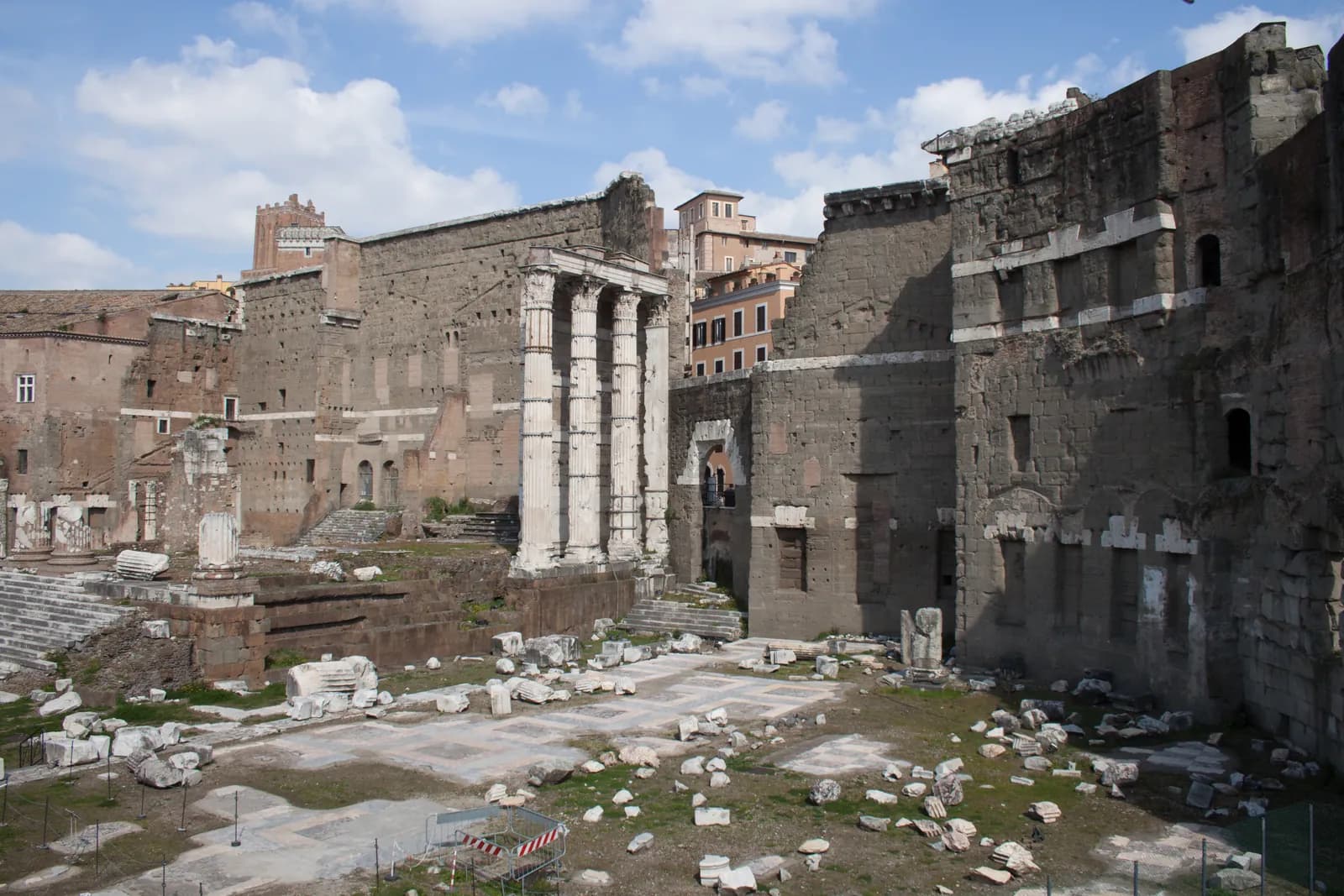 Three tall columns on a high stepped podium standing in front of an enormous plain wall of grey stone blocks.