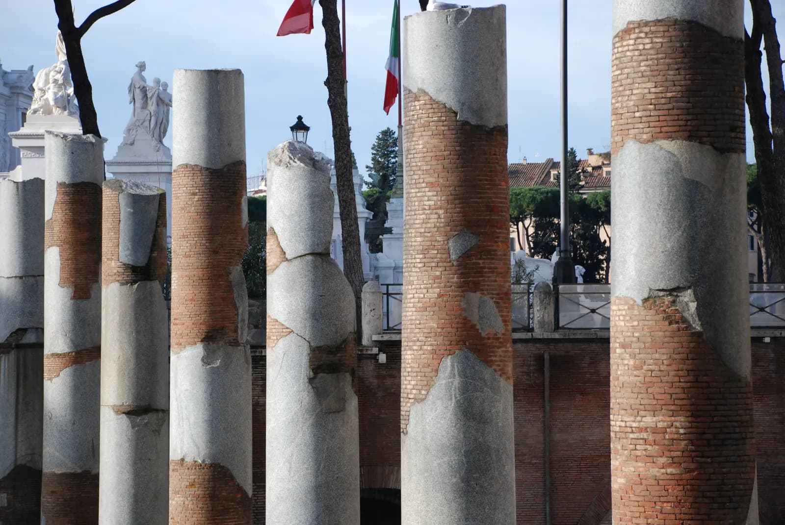 An excavated hollow below modern street level containing rows of grey granite column stumps and paving, with brick buildings beyond.